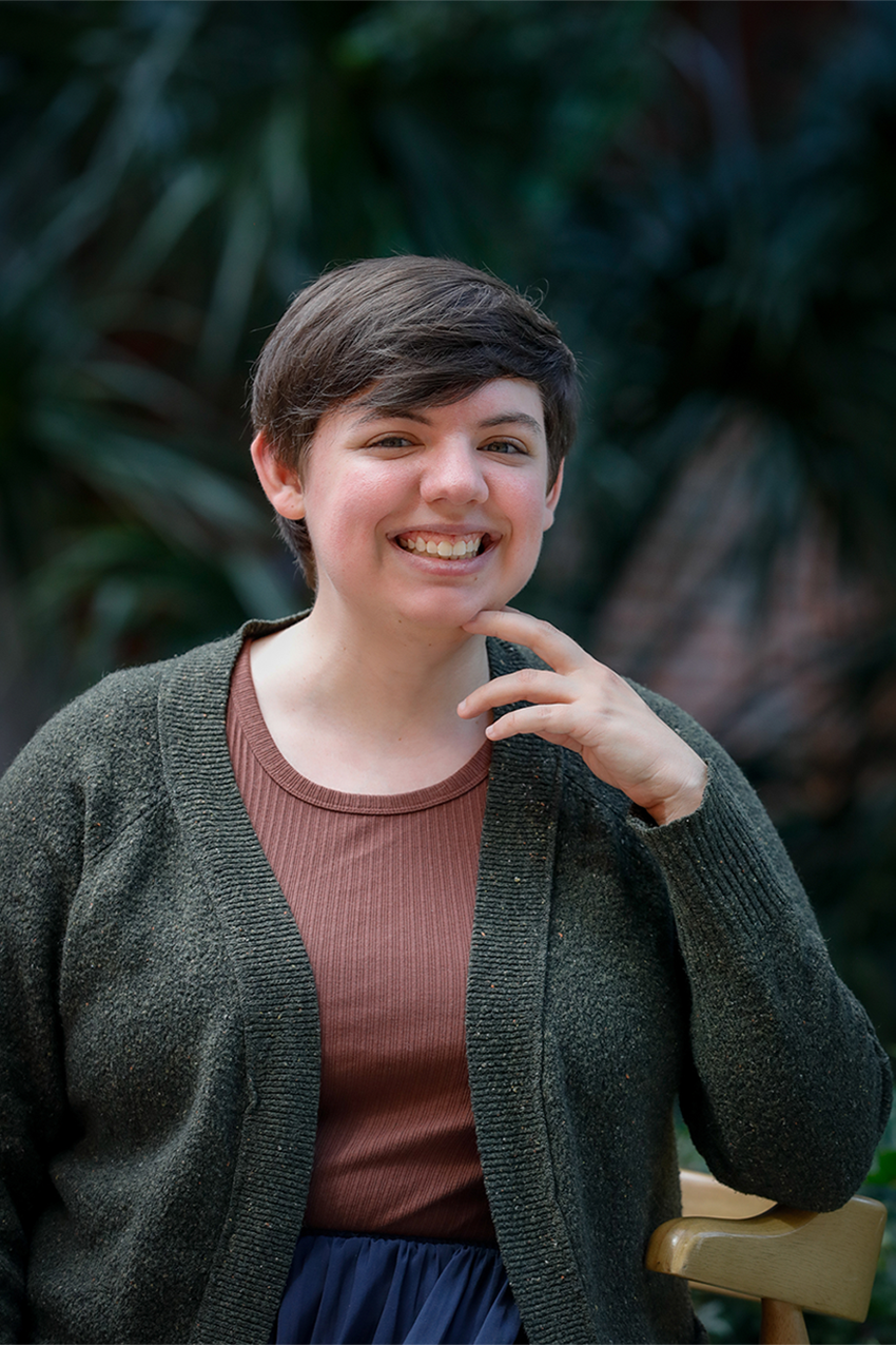 Portrait of Katherine Heneghan smiling with their hand brushing against their face