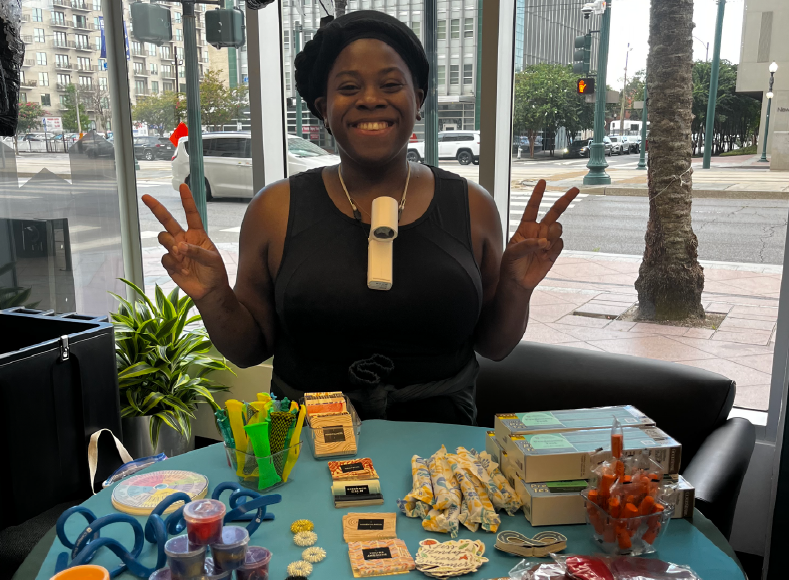 Natasha of The Well smiling and posing with "peace sign" fingers at a tabling Downtown