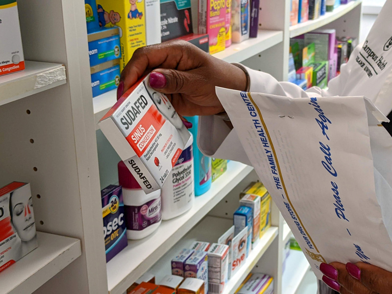 Pharmacist holding Sudafed in front of shelf with OTC products